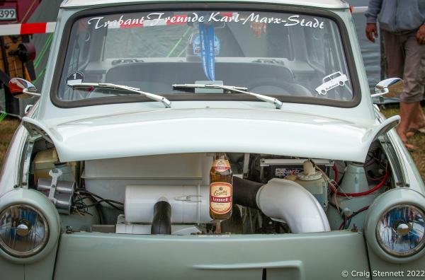 ZWICKAU, GERMANY- AUGUST 31: The inner workings of the Iconic East German Trabant propped open with a beer bottle at the Trabant Club Zwickau annual gathering of Trabi owners in 2018. The engine for the 500, 600 and the original 601 was a small two-stroke engine with two cylinders, accounting for the vehicle&#39;s modest performance. Its curb weight was about 600 kilograms (1,323 lb). When it ceased production in 1989, the Trabant delivered 19 kilowatts (25 hp) from a 600 cc (37 cu in) displacement. It took 21 seconds to accelerate from zero to its top speed of 100 km/h (62 mph). The engine produced a very smoky exhaust and was a significant source of air pollution: nine times the hydrocarbons and five times the carbon-monoxide emissions of the average 2007 European car. Its fuel consumption was 7 l/100 km (40 mpg‑imp; 34 mpg‑US). Since the engine did not have an oil pump, two-stroke oil had to be added to the 24-liter (6.3 U.S. gal; 5.3 imp gal) fuel tank[13] at a 50:1 (or 33:1) ratio of fuel to oil at each fill-up. Contemporary gas stations in countries where two-stroke engines were common sold a premixed gas-oil mixture at the pump. Because the Trabant had no fuel pump, its fuel tank was above the motor so fuel could reach the carburetor by gravity; this increased the risk of fire in front-end accidents. Earlier models had no fuel gauge, and a dipstick was inserted into the tank to determine how much fuel remained. Best known for its dull color scheme and cramped, uncomfortable ride, the Trabant is an object of ridicule for many Germans and is regarded as symbolic of the fall of the Eastern Bloc. Known as a &quot;spark plug with a roof&quot; because of its small size, the car did gain public affection. Its design remained essentially unchanged from its introduction in the late 1950s, and the last model was introduced in 1964. In contrast, the West German Volkswagen Beetle received a number of updates (including improvements in efficiency) over a similar period. (Photo by