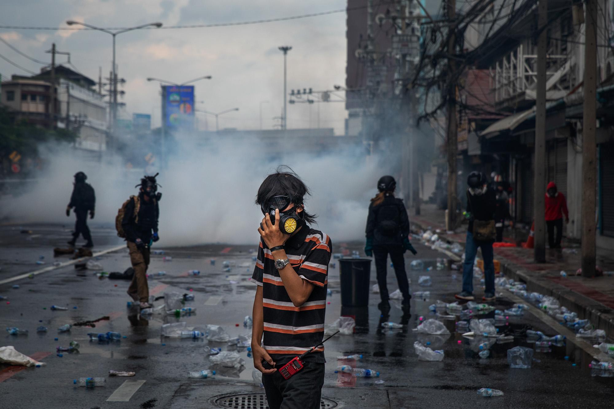 Pro-democracy protestors react to tear gas from riot police during a rally near Din Daeng intersection in Bangkok, Thailand, August 2021. This day marked the beginning of an escalation in violent protests that continued through the rest of the year, primarily located around the Din Daeng area. 