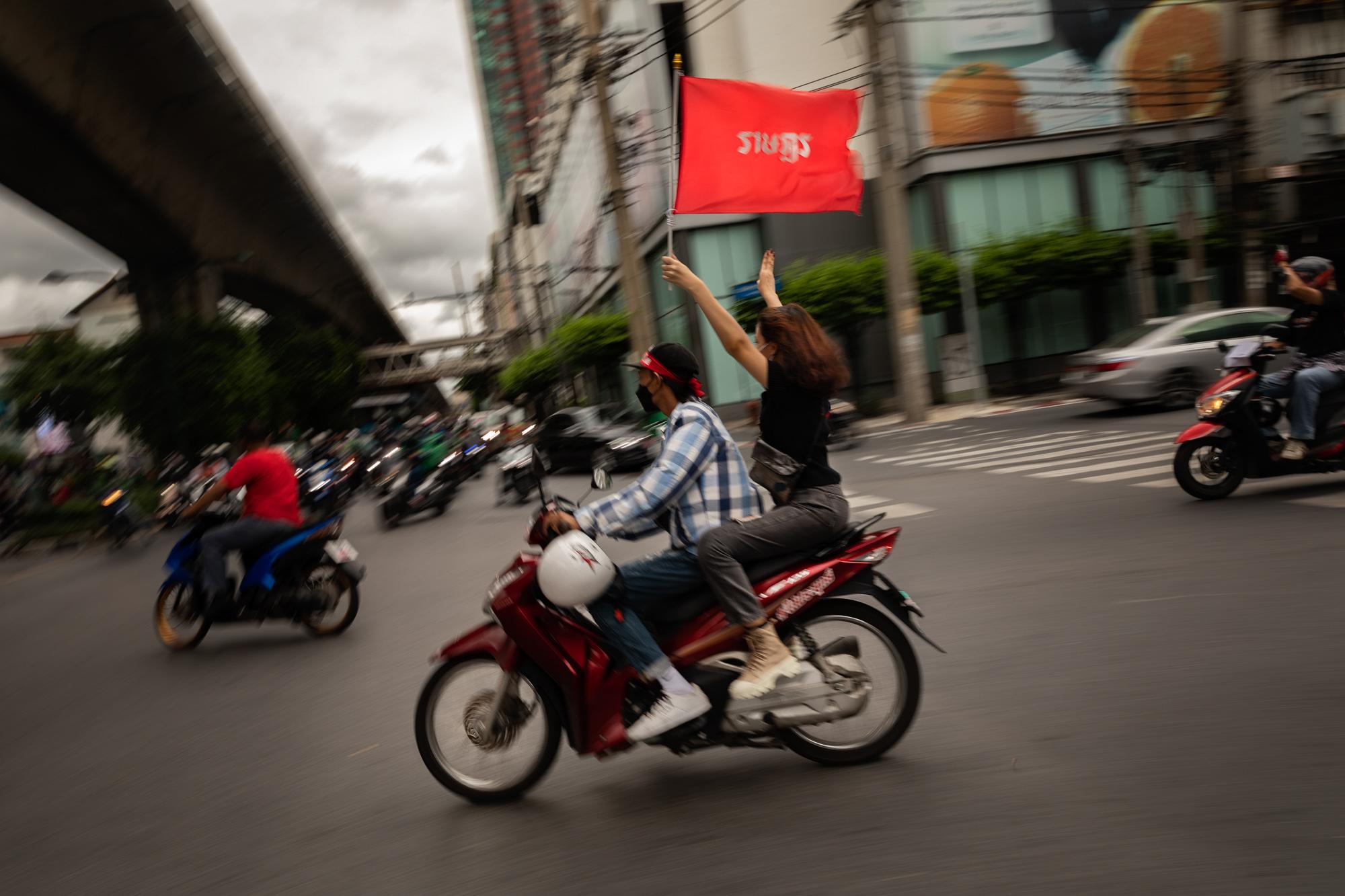 A pro-democracy protestor holds up a sign reading &quot;Ratsadon&quot; during a motorbike rally from Ratchaprasong intersection to Victory Monument in Bangkok, Thailand, August 2021. The Ratsadon protest group is a reference to Khana Ratsadon (The People&#39;s Party), founded in 1926, that organized a peaceful revolution against King Prajadhipok, leading the country from an absolute monarchy into a constitutional monarchy.