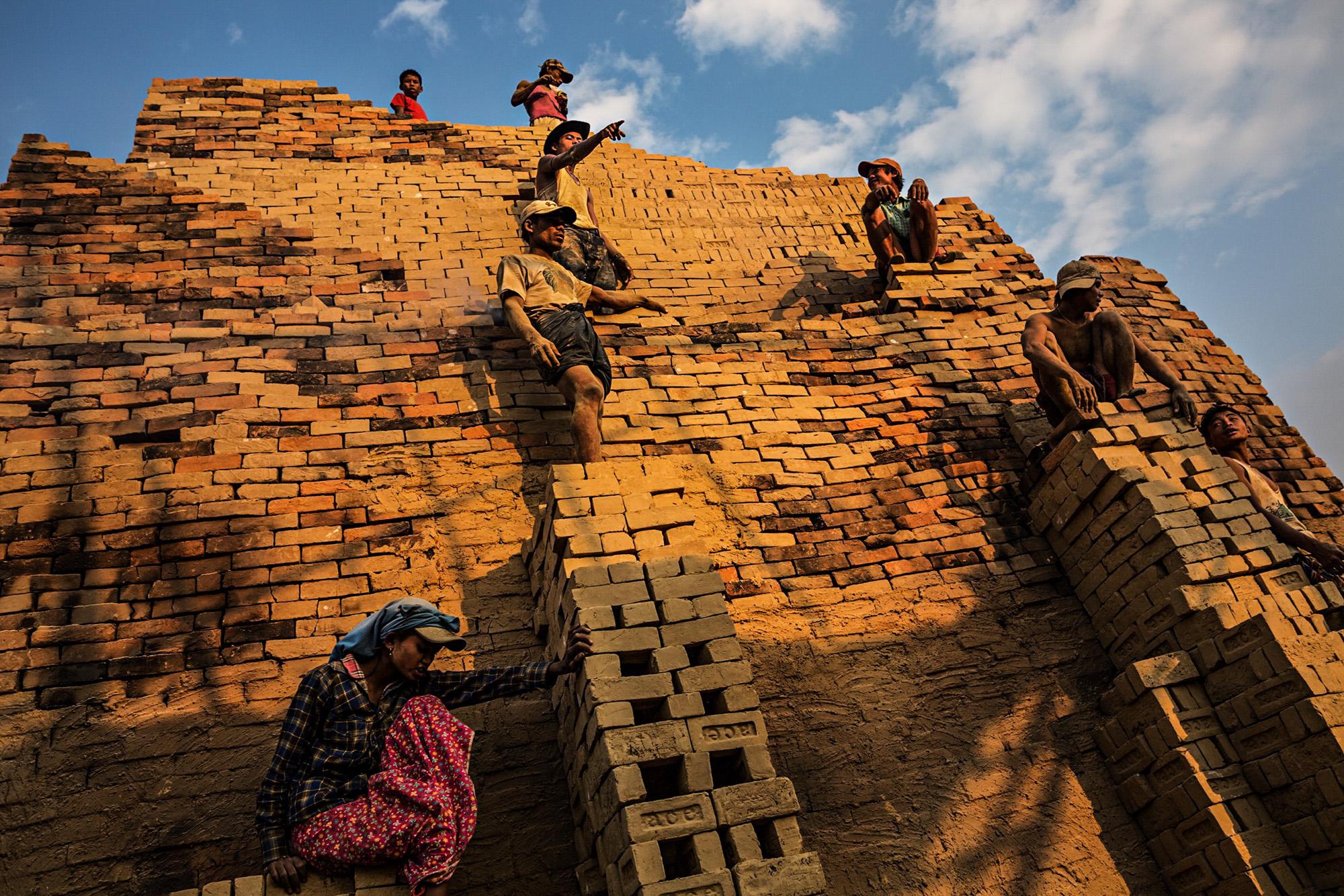  Workers stand on the face of a brick kiln in order to move bricks from the bottom to the to the top of the kiln, on the outskirts of Yangon, Myanmar, January 2015. 