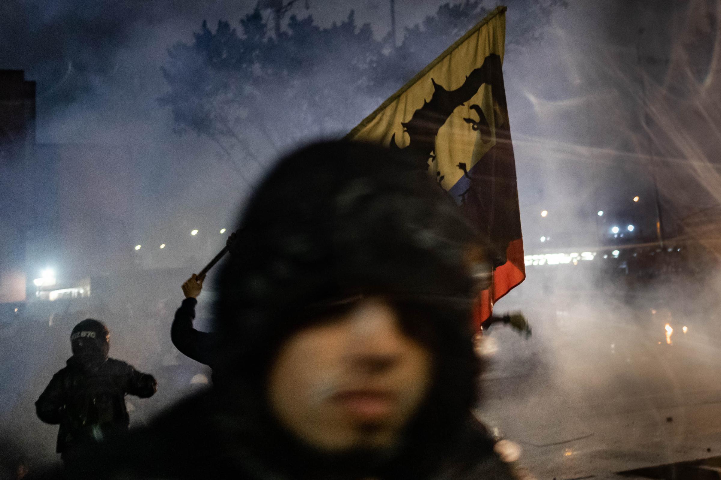 2021 in pictures - A protester runs amidst a cloud of teargas while carrying a flag emblazoned with the face of Che...