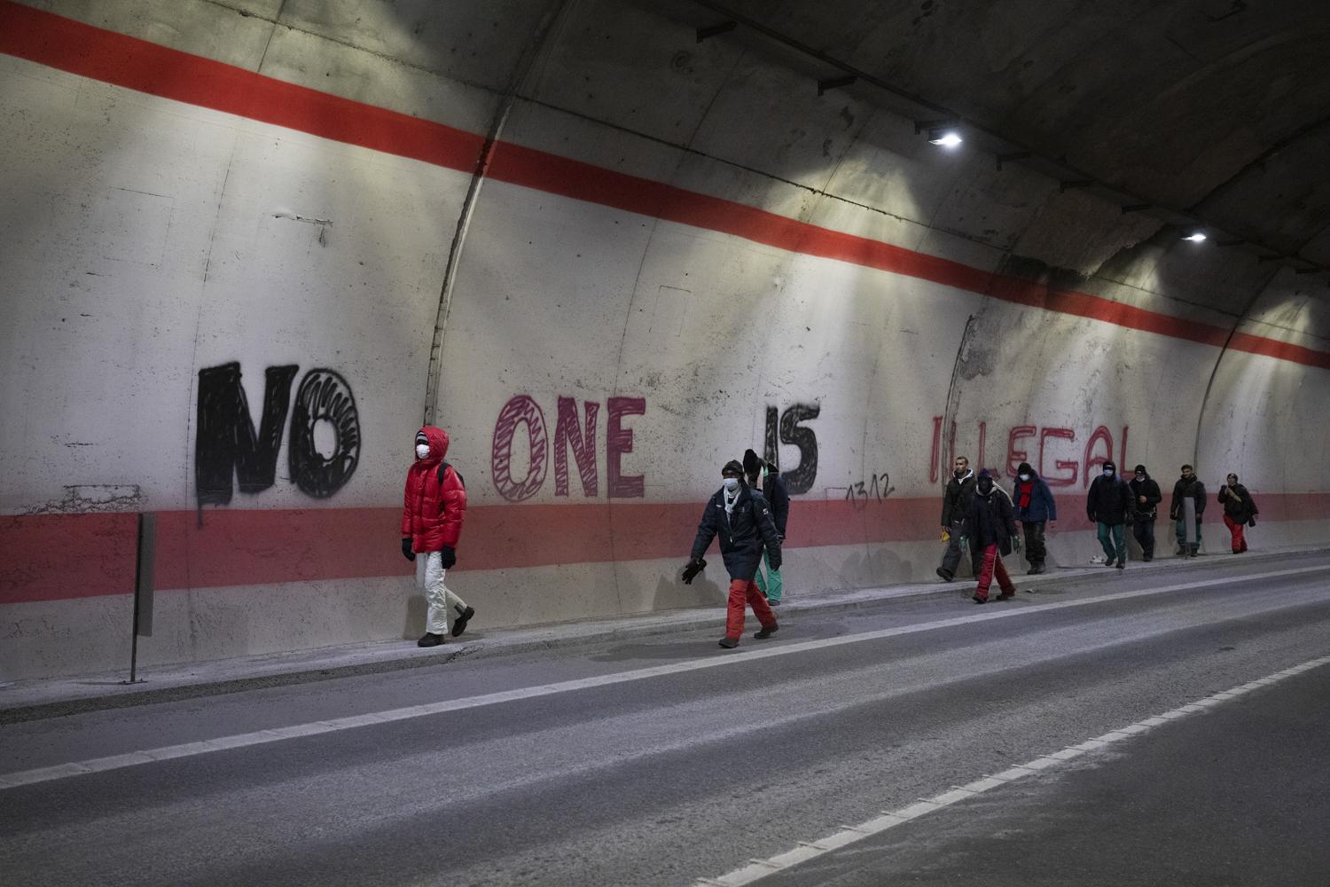 Migrants headed to France from Italy walk by a grafitti that reads “no one is illegal” in a...