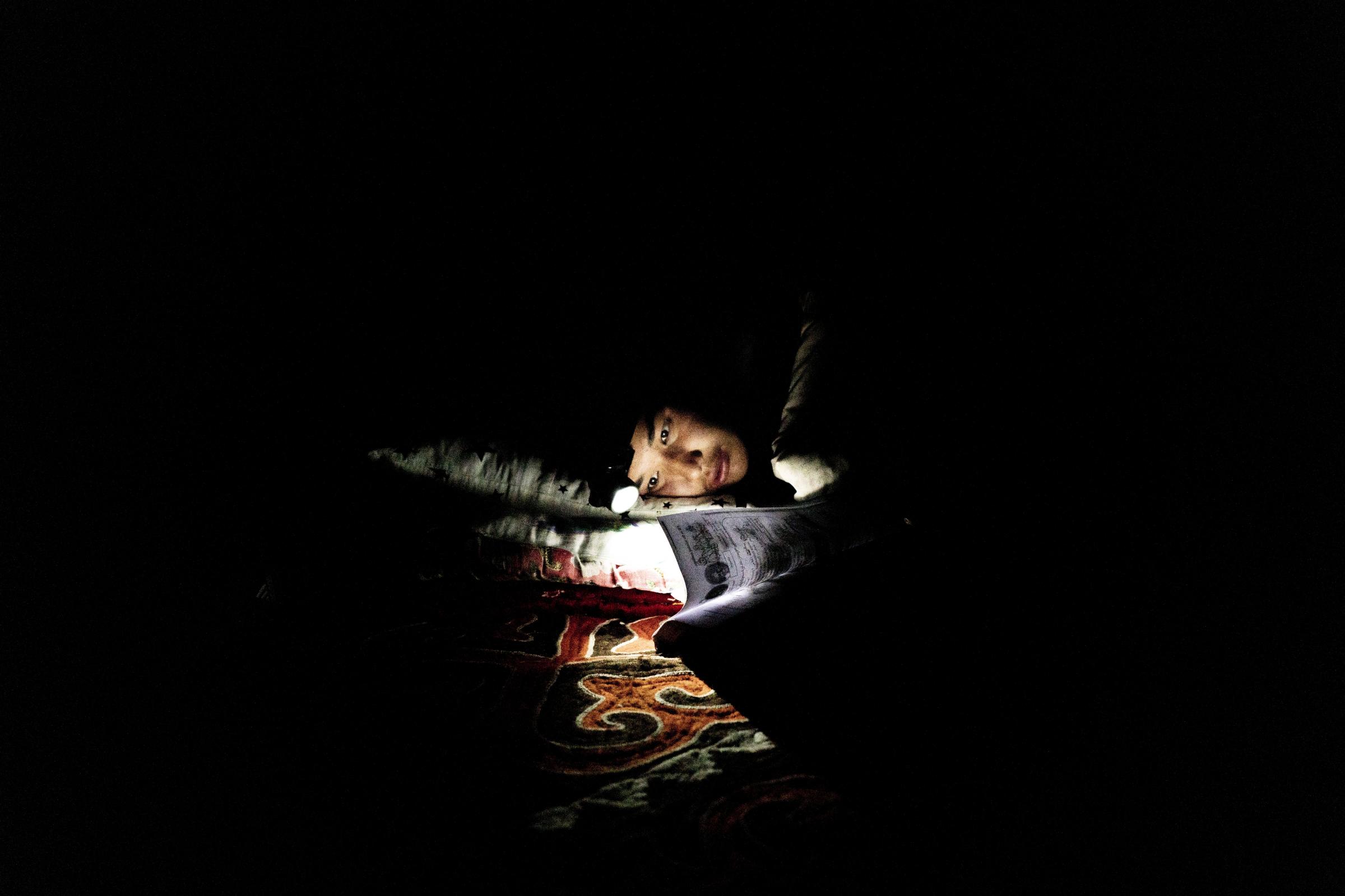Nomads - Myrbek studies a German textbook by headlamp before bed. He has taken to studying German in hopes...