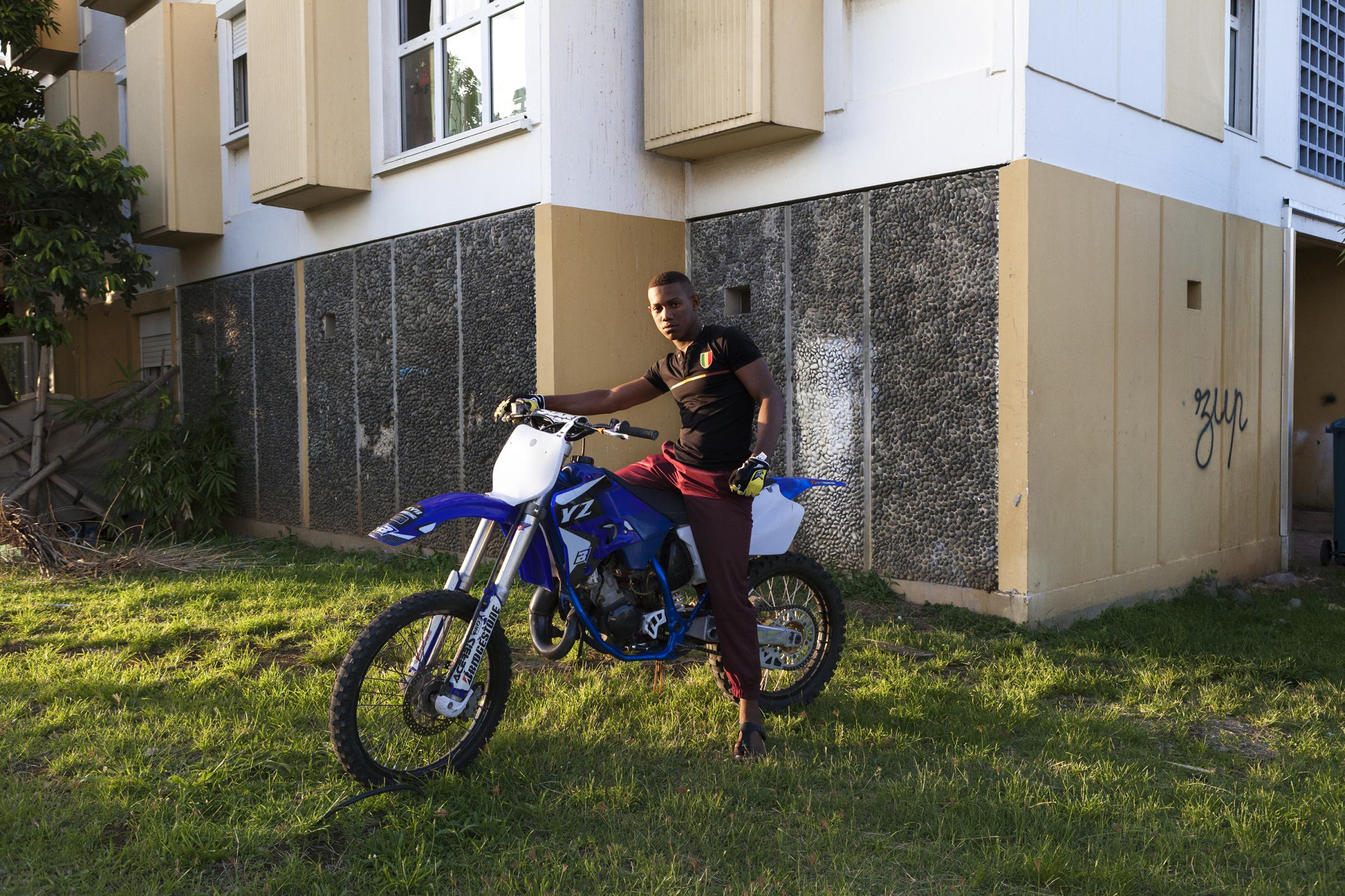 • Kartié Dom-Tom -  Portrait d’un jeune sur sa moto devant son...