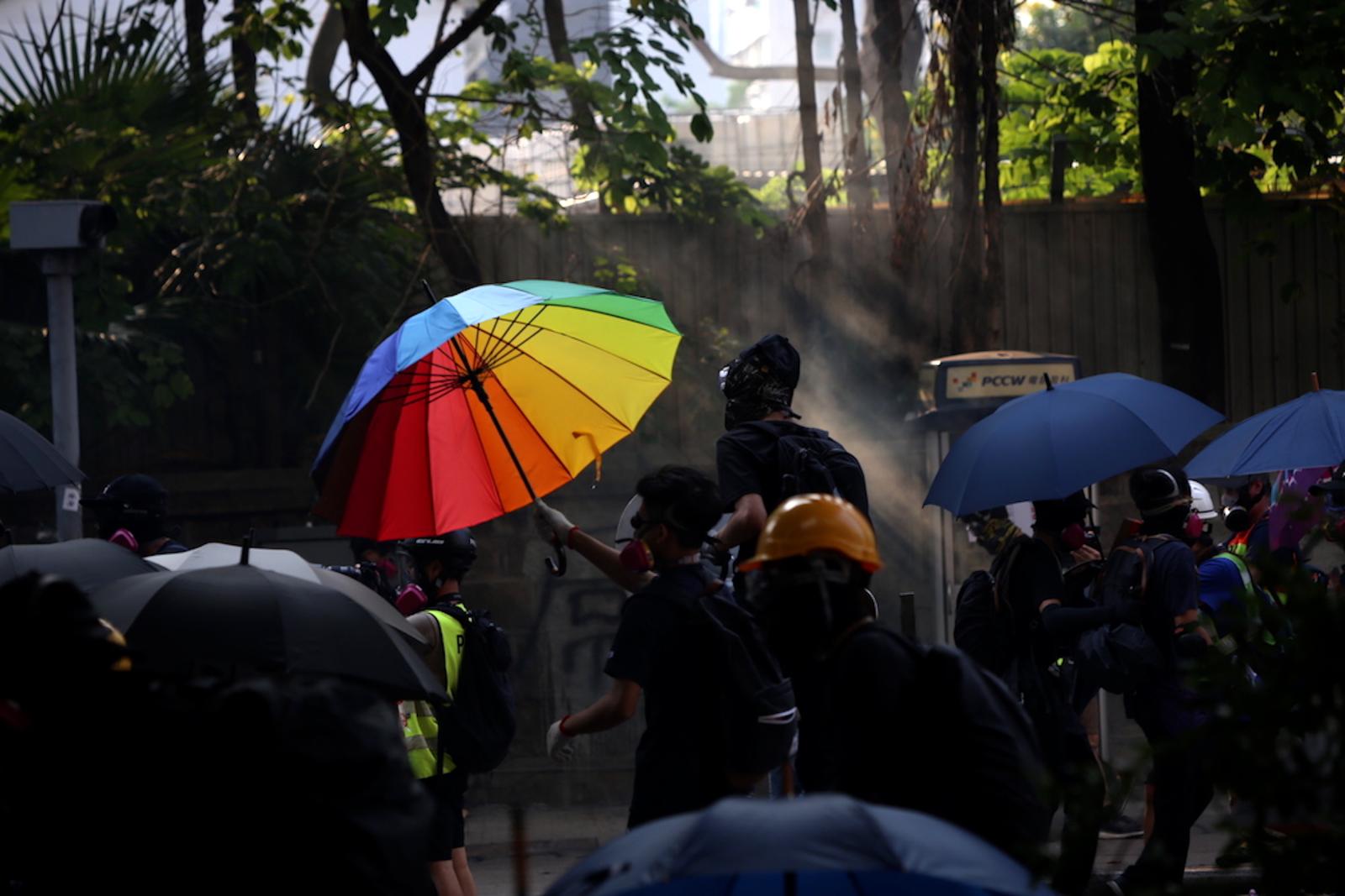  Tsim Sha Tsui, Hong Kong (October 20, 2019) - A black-clad protestor uses a bright umbrella as a shield against tear gas and surveillance as they pass by a police station. 