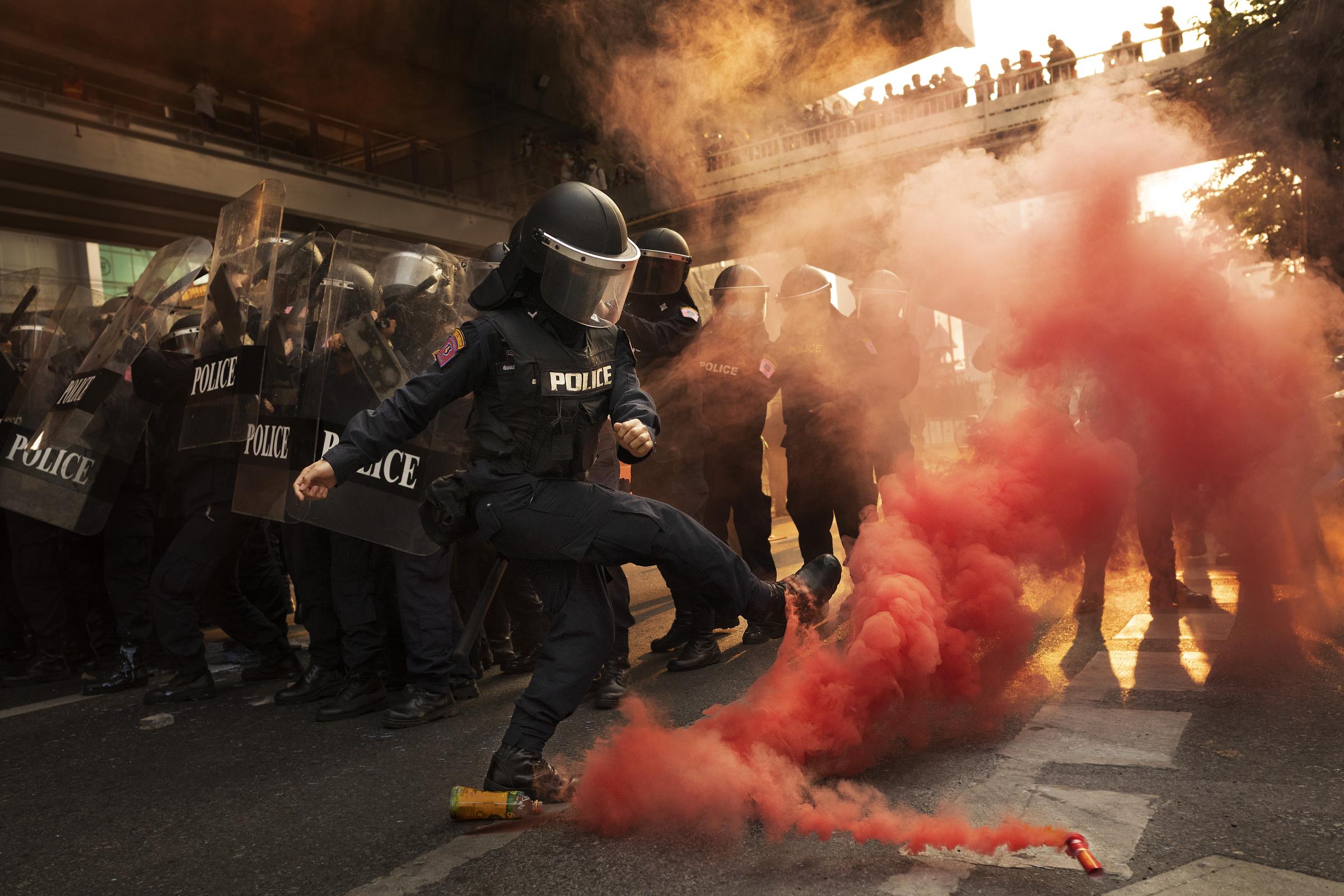 A Thai riot police officer kicks a smoke bomb out of the road during a clash with anti-government protestors in Bangkok, Thailand, February 2021.