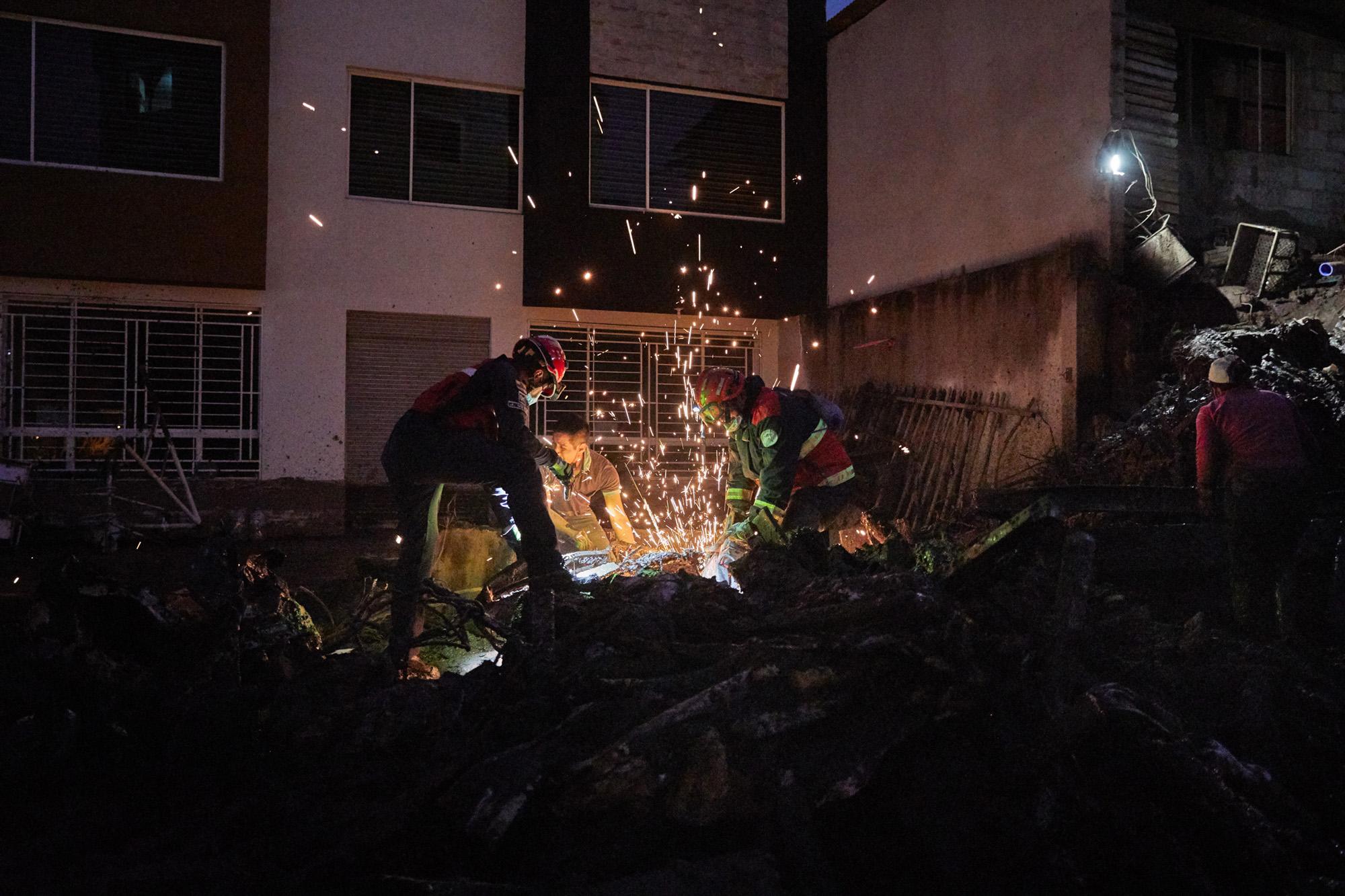 Members of rescue teams remain on the job until nightfall, 24 hours after a mudslide in Quito,...