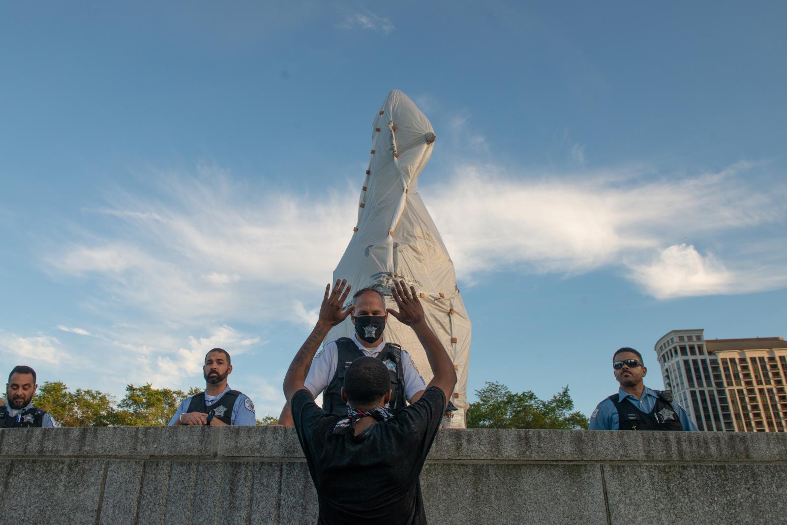 The Storming of the Columbus Statue  - A protestor confronts the Police protecting the Columbus Statue, Raising his hands in a...