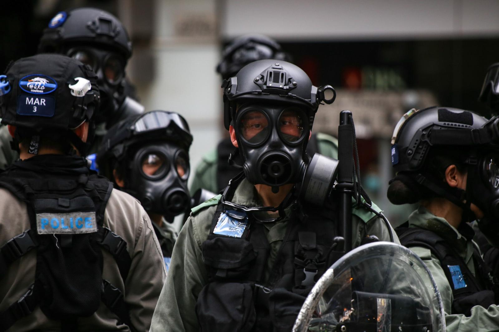 A young police officer looks into a crowd of journalists, with his gas mask askew on his face. Since the eruption of protests in Hong Kong from 2019-2020, the reputation of Hong Kong police have dropped to its lowest point, receiving the least popularity of all disciplinary forces.