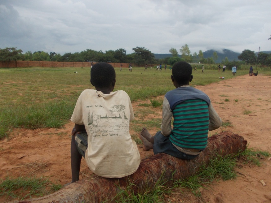 Two boys watch a game of footba...i, near the border with Zambia.