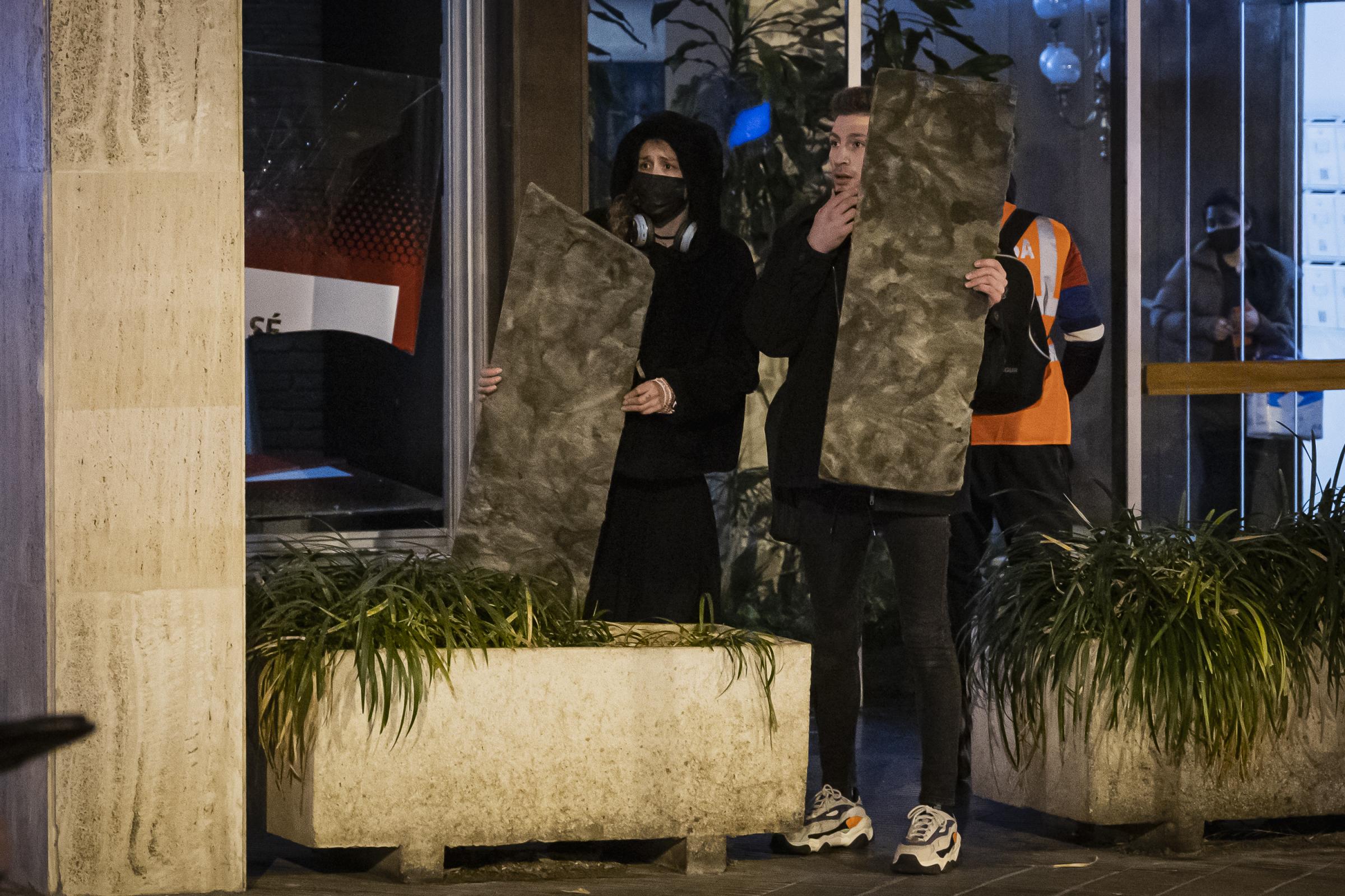 Two young, removed from the clashes between police and demonstrators, protect themselves with...