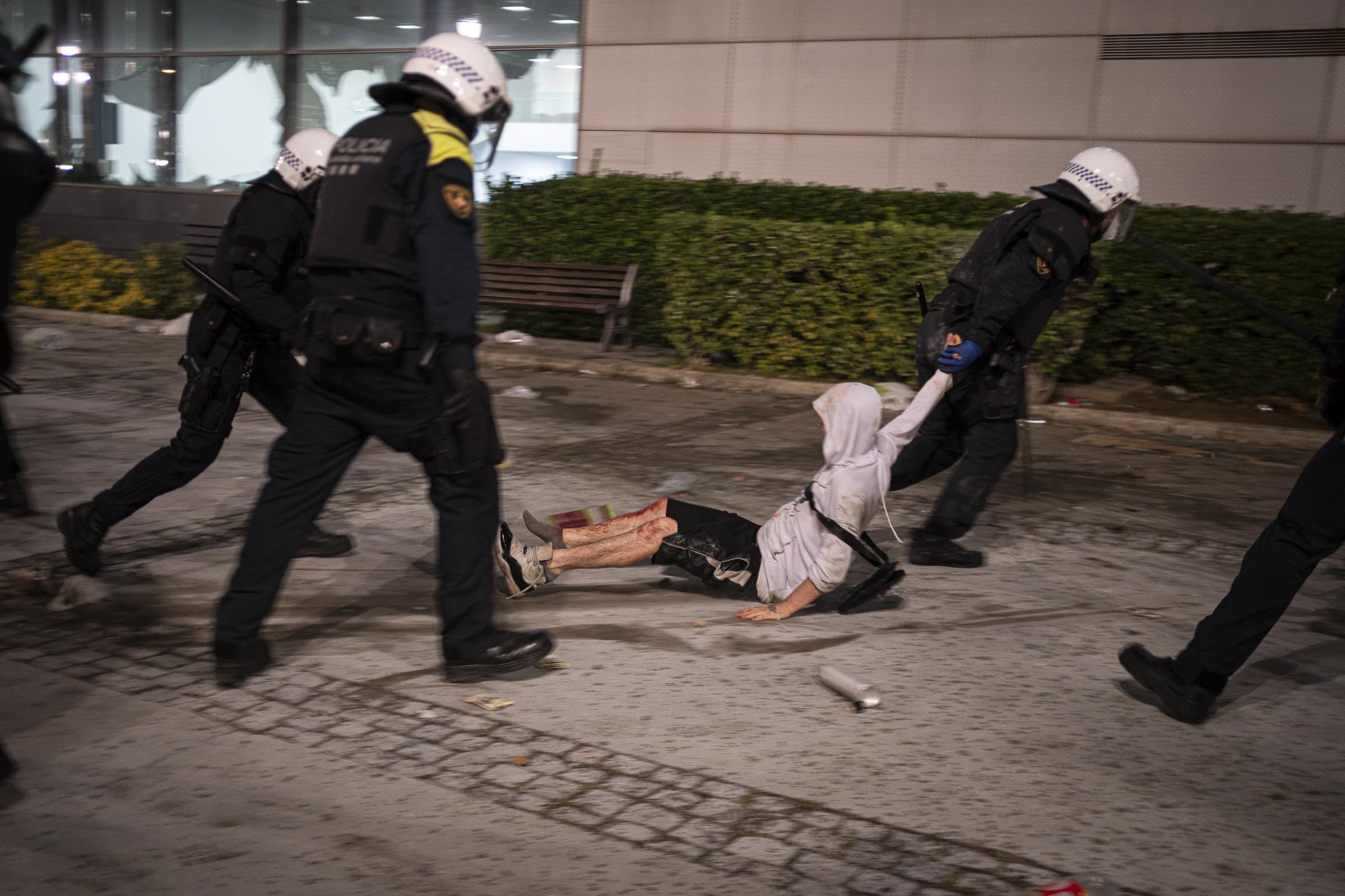 A young man, his legs bloodied, is dragged by a Guardia Urbana anti-riot police officer into the...